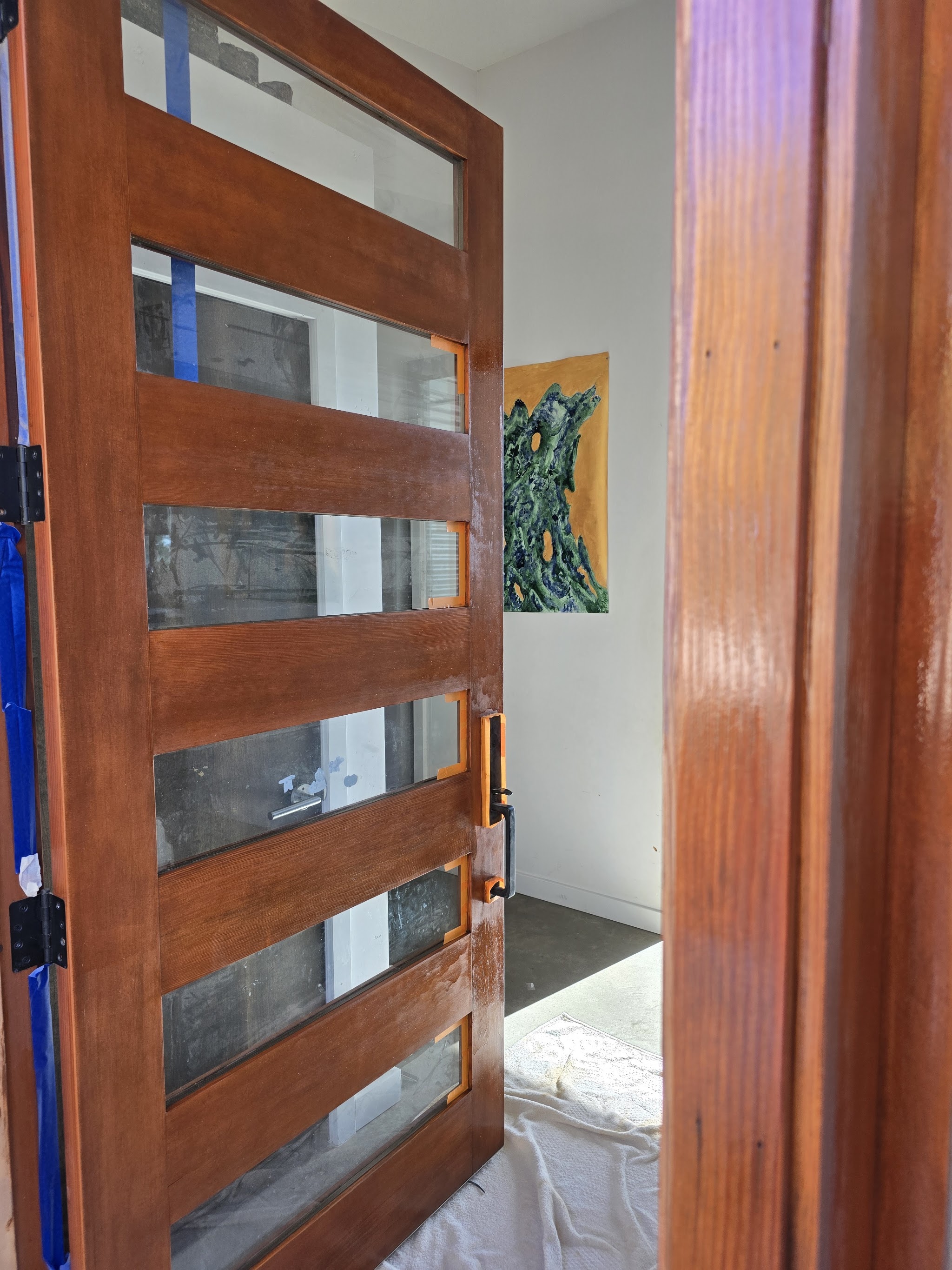 Wood door being stained with painter's tape along the glass edges